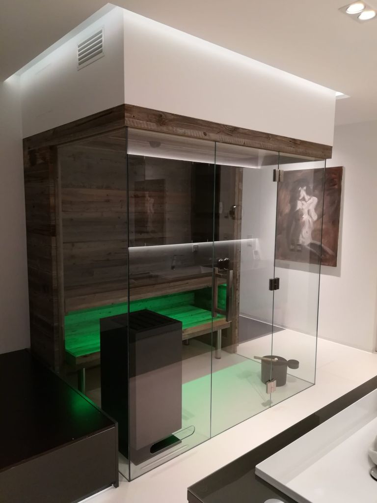Sauna mit Altholz-Verkleidung, ganzflaechiger Glasfront und gruener Ambiente-Beleuchtung