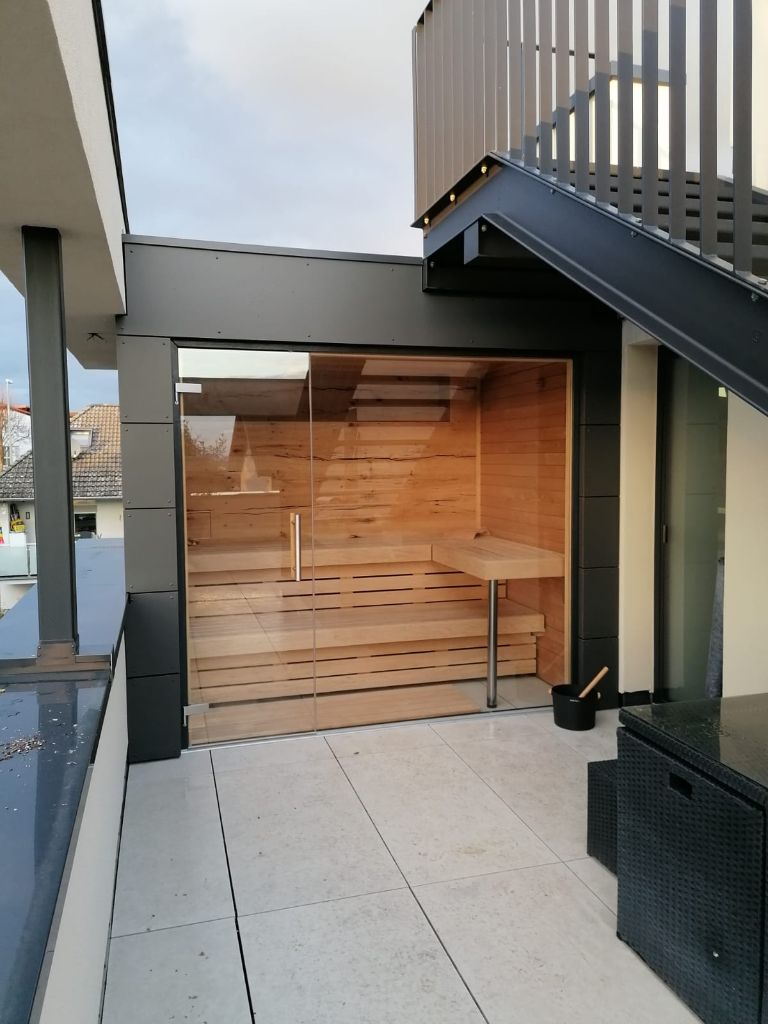 Outdoor-Sauna mit Glasfront auf einem Balkon, dunkle Metallfassade